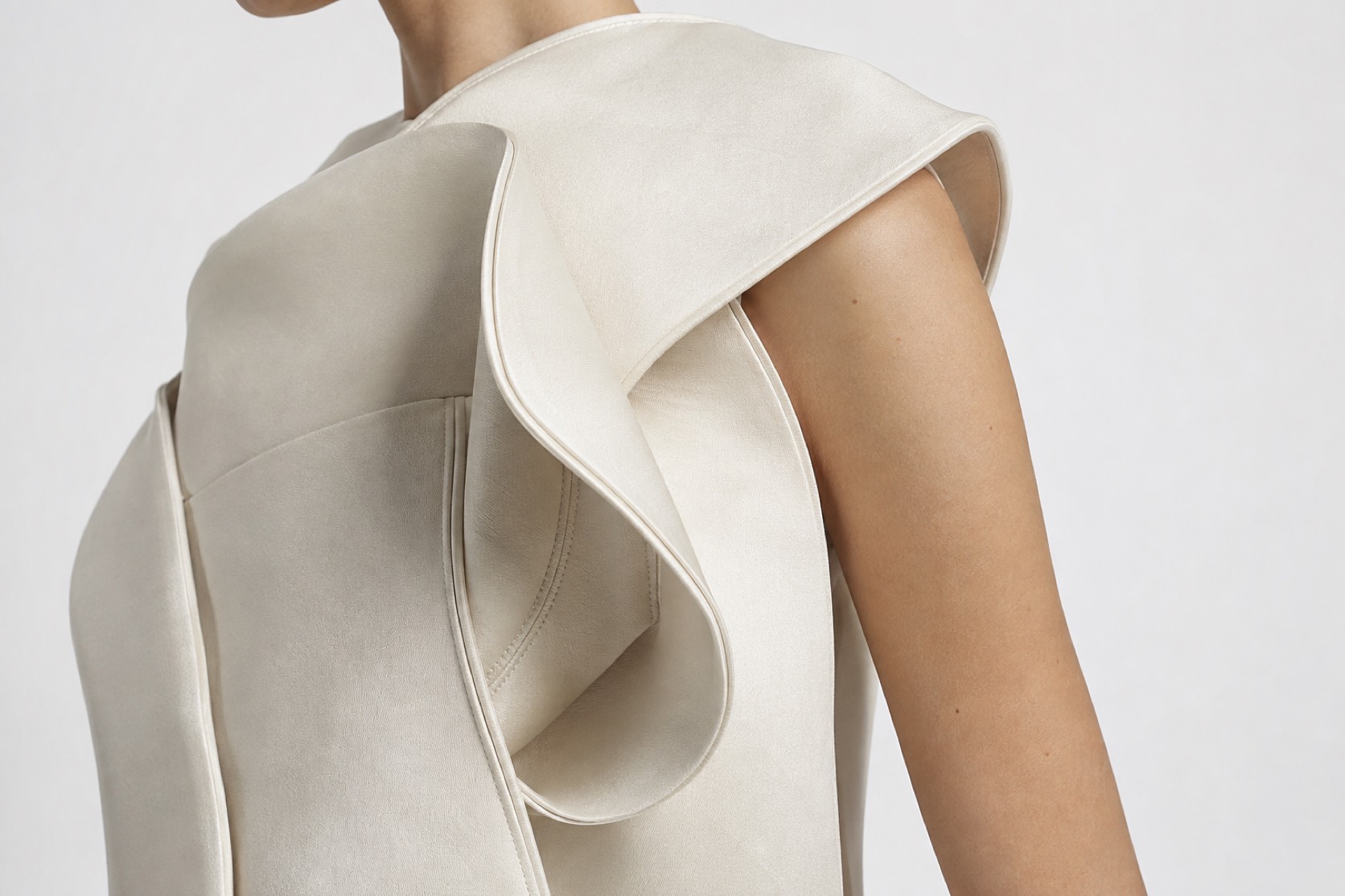 Close view of an ivory garment’s curved folded seam and hollow fabric volume.
