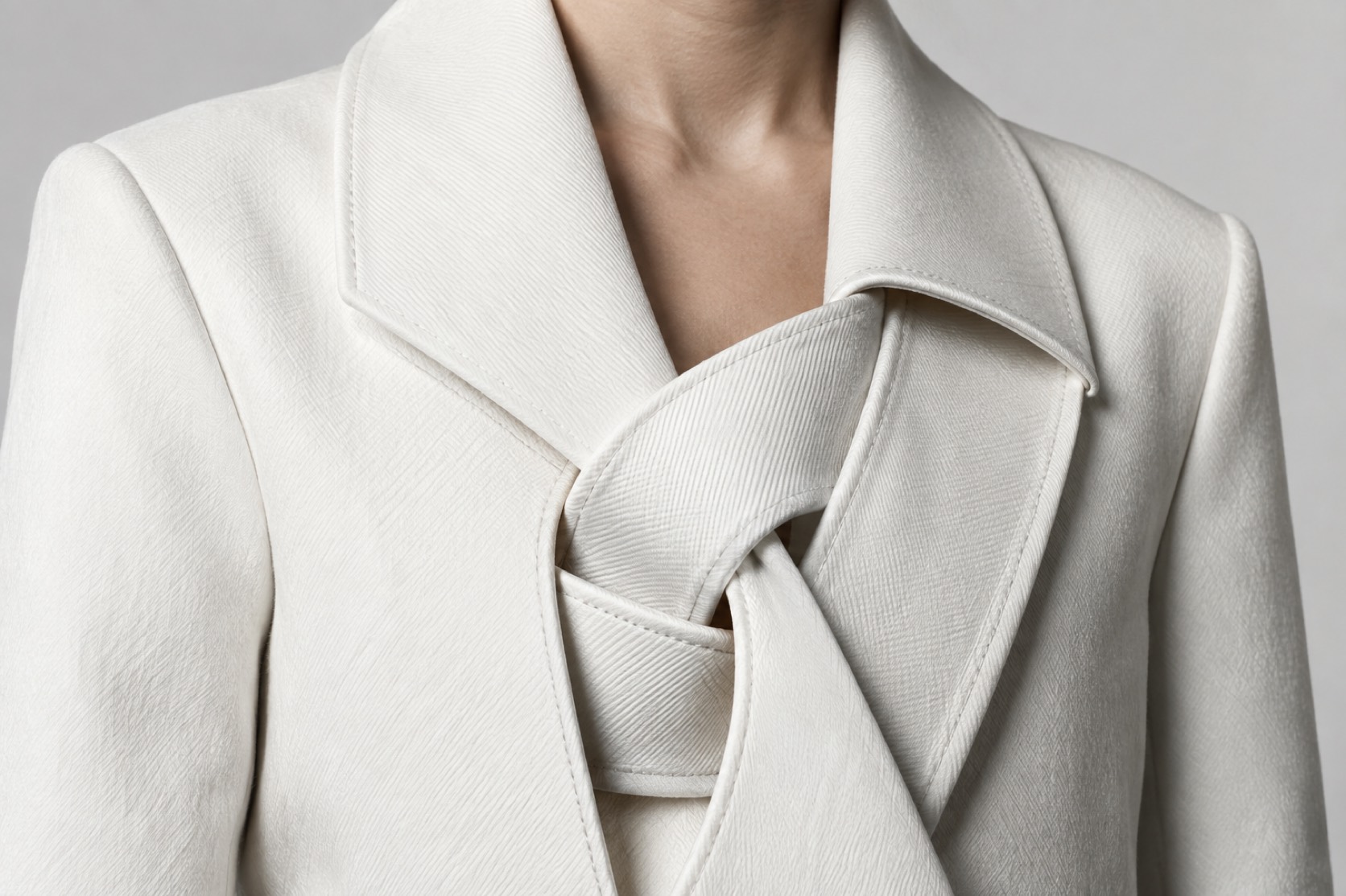 Interwoven white lapel bands create a sculptural opening in a tailored coat.