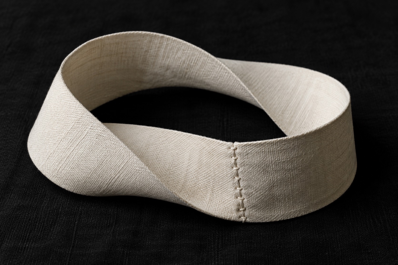 A stitched strip of ivory cloth forms a twisted loop on black fabric.